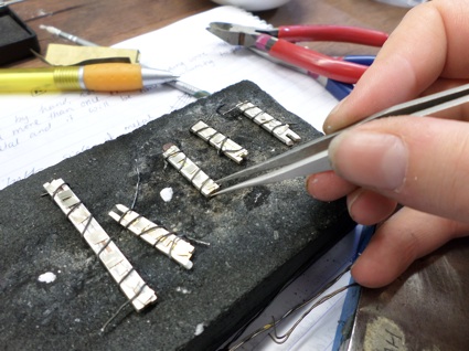 Placing solder on the wires (held together with binding wire) to create precious metal mosaic patterns.